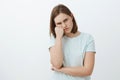 Studio shot of displeased offended and gloomy cute female brunette in t-shirt leaning face on fist frowning and pursing