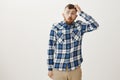 Studio shot of dumb handsome man in plaid shirt and falling glasses, scratching head and folding lips while saying wow Royalty Free Stock Photo