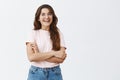 Studio shot of emotive and joyful carefree brunette girlfriend with long hair in glasses and jeans holding hands crossed