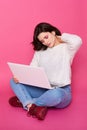 Studio shot of exhausted female with pain in neck, holding white lap top on her knee while sitting on floor, keeps eyes closed, Royalty Free Stock Photo