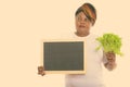 Studio shot of fat black African woman thinking while holding lettuce and blank blackboard Royalty Free Stock Photo