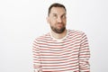 Studio shot of funny childish bearded man in striped pullover, making faces or aping, looking up with squinted eyes and Royalty Free Stock Photo
