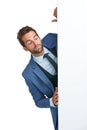 Proceed with caution. Studio shot of a handsome businessman peering around a wall against a white background.