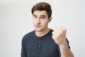 Studio shot of handsome european male model showing fist to camera and lifting eyebrows, demanding something over gray Royalty Free Stock Photo