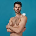 Studio shot of handsome naked brunette guy posing with white jar of effective cream on his shoulder, looking at camera