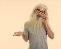 Studio shot of senior bearded man thinking while looking confused and talking on mobile phone Royalty Free Stock Photo