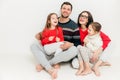 Studio shot of happy family members sit on floor with bare feet, embrace each other, have joyful expression, laugh as hear