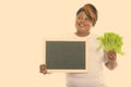 Studio shot of happy fat black African woman smiling and thinking while holding lettuce and blank blackboard Royalty Free Stock Photo
