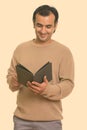 Studio shot of happy Persian man smiling and reading book Royalty Free Stock Photo