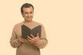 Studio shot of happy Persian man smiling and reading book Royalty Free Stock Photo