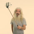 Studio shot of happy senior bearded man smiling while taking selfie picture with mobile phone on selfie stick Royalty Free Stock Photo