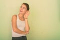 Studio shot of happy teenage girl smiling while thinking and listening against green painted wall Royalty Free Stock Photo