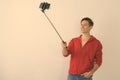 Studio shot of happy young handsome man smiling while taking selfie picture with mobile phone on selfie stick against Royalty Free Stock Photo