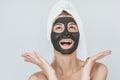 Studio shot of happy young woman with facial cosmetic black organic clay mask on her face, looks up to advertising text, wears Royalty Free Stock Photo