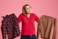 Studio shot of hesitant indecisive young Cucasian woman holds two items of clothes, cant decide what to wear this day, likes