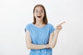 Studio shot of impressed happy european girl in casual clothes, pointing right and smiling broadly, being fascinated