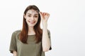 Studio shot of joyful beautiful urban female student taking off trendy round glasses and holding eyewear on forehead