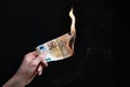 Studio shot of left hand holding a burning fifty Euro bank note. Concept for inflation, eurozone crisis, economic