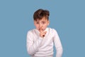 Studio shot of little boy holding his index finger at his lips asking this gesture not to reveal secrets