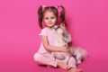 Studio shot of little funny child sitting on floor, looking directly at camera, hugging her pet, dog enjoying time with kid, sweet Royalty Free Stock Photo