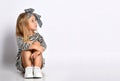 Studio shot little girl in a striped dress and hair band. Sits on the floor and looks towards the place for your advertisement