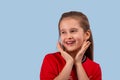 Studio shot of smiling girl wearing red shirt on a blue background. She looks away, touching the finger of both hands Royalty Free Stock Photo