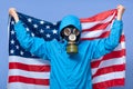 Studio shot of man ecologist holding USA flag behind him, wearing uniform and gas mask, posing isolated over blue background, Royalty Free Stock Photo