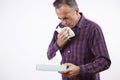 Studio Shot Of Mature Man With Cold Or Flu Virus Sneezing Into Paper Tissue Against White Background Royalty Free Stock Photo