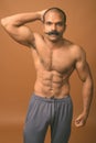 Muscular Indian man with mustache shirtless against brown background