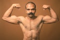 Muscular Indian man with mustache shirtless against brown background