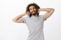 Studio shot of musculine confident hispanic guy with joyful attitude and curly hair, holding hands behind head and