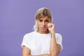 Studio shot of offended sad and timid silly woman with blond hairstyle frowning looking from under forehead holding fist