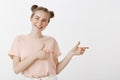 Studio shot of optimistic happy feminine european woman with cute buns hairstyle and freckles, pointing right with