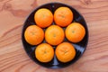 Top view of 7 orange fruit citrus tankan on black dish against wooden background