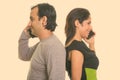 Happy Persian couple smiling while talking on mobile phone together back to back Royalty Free Stock Photo