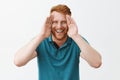 Studio shot of playful and joyful good-looking young redhead father with bristle holding palms along face and smiling