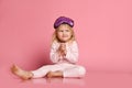 Studio shot of pleased beautiful young woman posing in eyemask. Cheerful Little cute girl in pajamas sits on the floor on pink Royalty Free Stock Photo