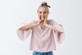 Studio shot of pleased grinning optimistic woman with blonde hair with headband and striped blouse squeezing cheeks with