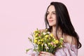 Studio shot of pleased woman with dreamy expression, dark hair, holds bouquet of flowers, thinks about something pleasant, poses Royalty Free Stock Photo