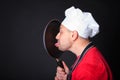 Studio shot of positive chef licks a frying pan.