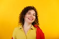 Studio shot of positive and smiling pretty female. Curly laughing girl in bright yellow shirt. Isolated on yellow