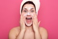 Studio shot of pretty girl with facial mask, surprised female with white towel on her head, lady having astonished expression,