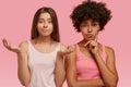 Studio shot of puzzled indecisive women spread palms, look doubtfully at camera, have make up their mind, stand next to