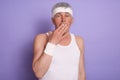 Studio shot of scared mature man wearing white t shirt and headband, looking directly at camera with big eyes, covering his mouth Royalty Free Stock Photo