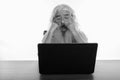 Studio shot of senior bearded man looking shocked while using laptop on wooden table Royalty Free Stock Photo