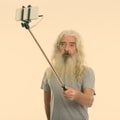 Studio shot of senior bearded man taking selfie picture with mobile phone on selfie stick Royalty Free Stock Photo