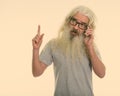 Studio shot of senior bearded man thinking while talking on mobile phone and pointing finger up Royalty Free Stock Photo