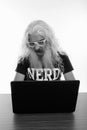 Studio shot of senior bearded nerd man looking shocked while using laptop on wooden table Royalty Free Stock Photo