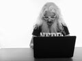 Studio shot of senior bearded nerd man wearing eyeglasses and looking shocked while using laptop on wooden table Royalty Free Stock Photo