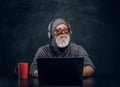 Contemporary elderly hacker with cup and laptop sitting at table